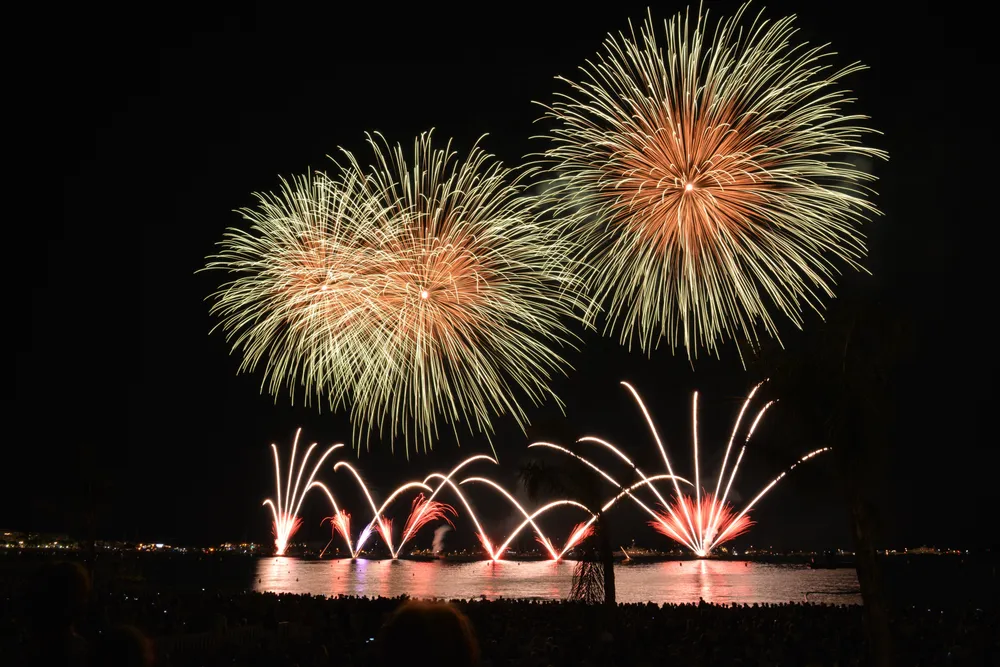 Spectacular multicoloured fireworks display over the sea in front of a crowded beach at night