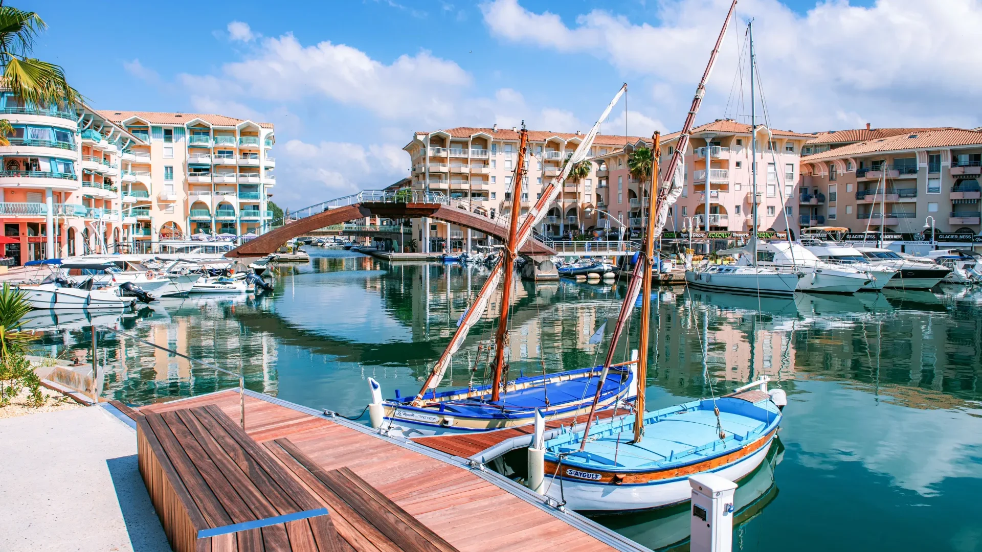 Arched wooden pedestrian footbridge over the water of a marina filled with yachts