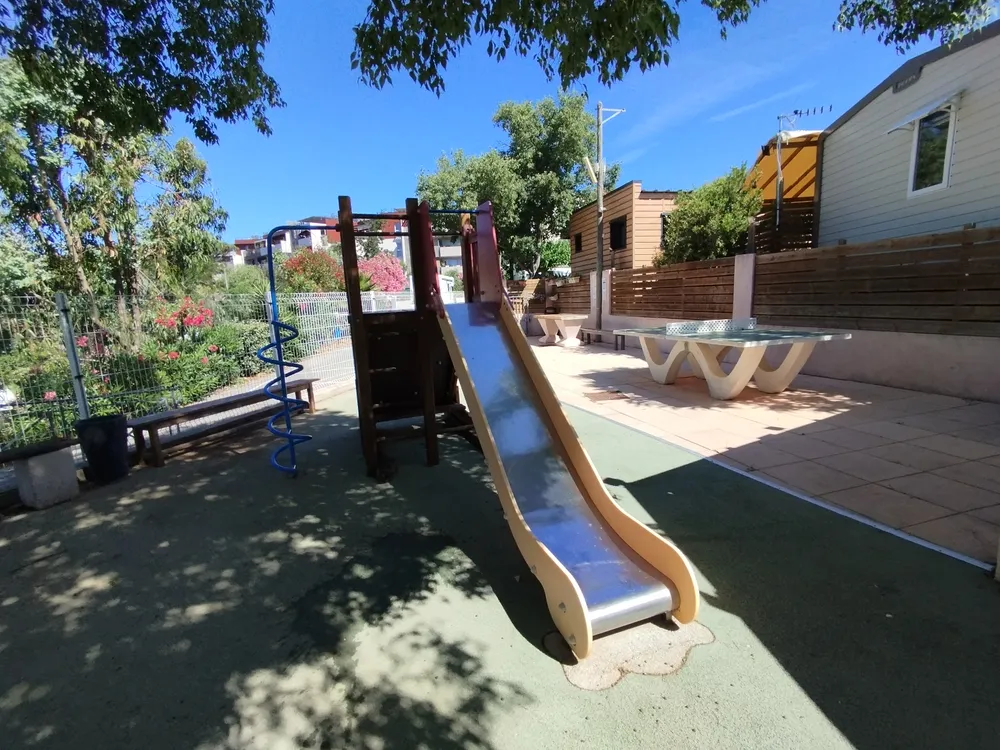 Outdoor play area including a slide and a ping-pong table under the sun