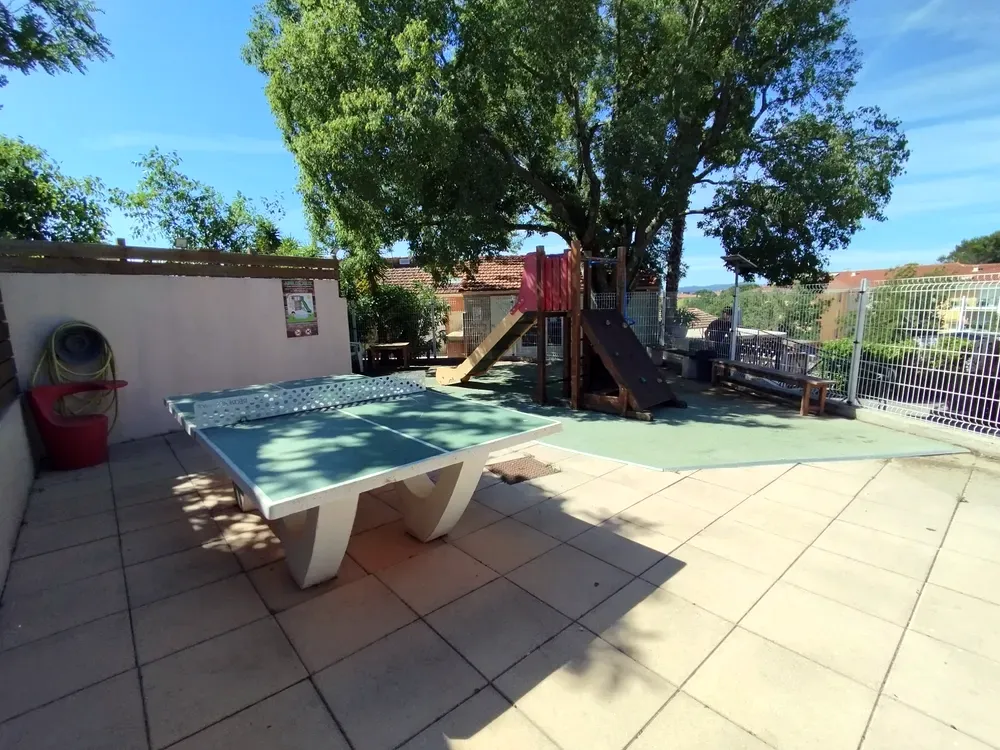Outdoor concrete ping-pong table and shaded playground area under a large tree
