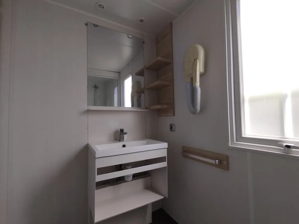 Mobile home bathroom with sink, vanity unit, mirror, and wall-mounted hair dryer.