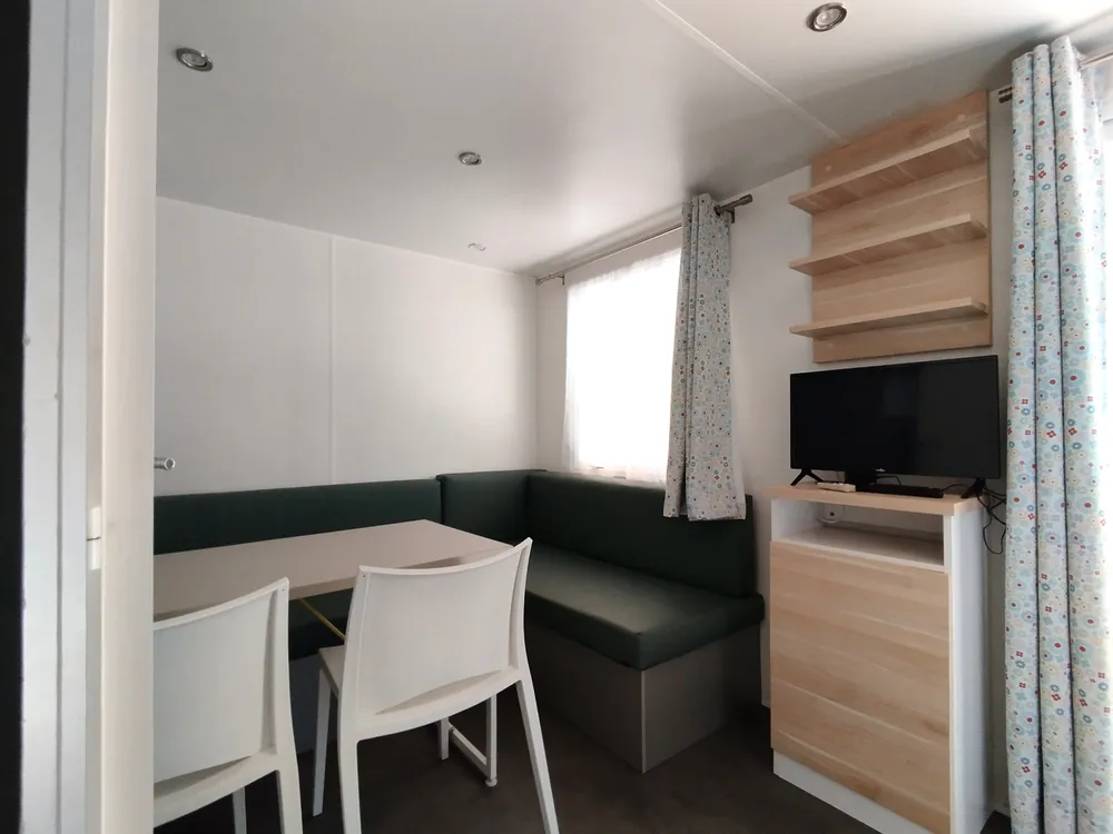 Interior living area of a mobile home featuring bench seating, dining table, chairs, and television.
