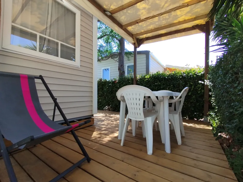 Covered wooden mobile home deck with table, chairs, and lounge chair.