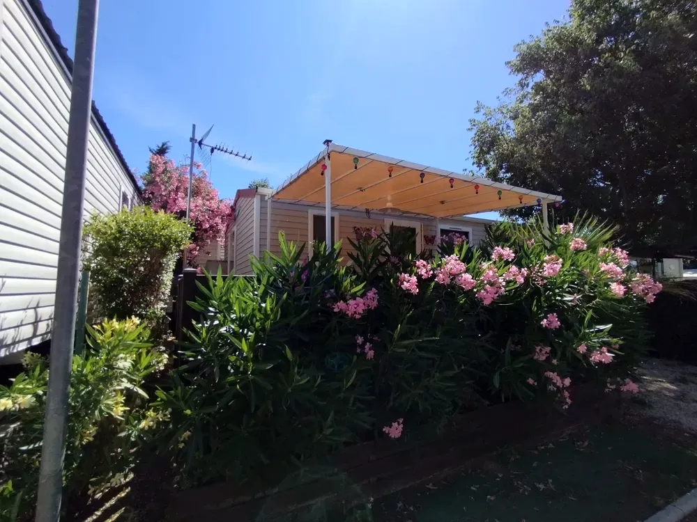 Beige mobile home with a large canvas awning and blooming oleanders