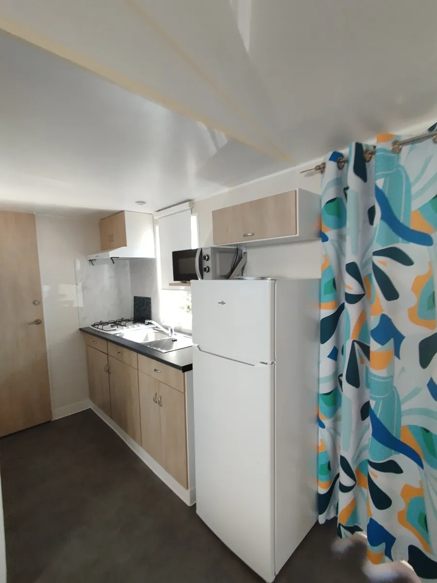 Perspective view of a linear mobile home kitchen with a colorful decorative curtain