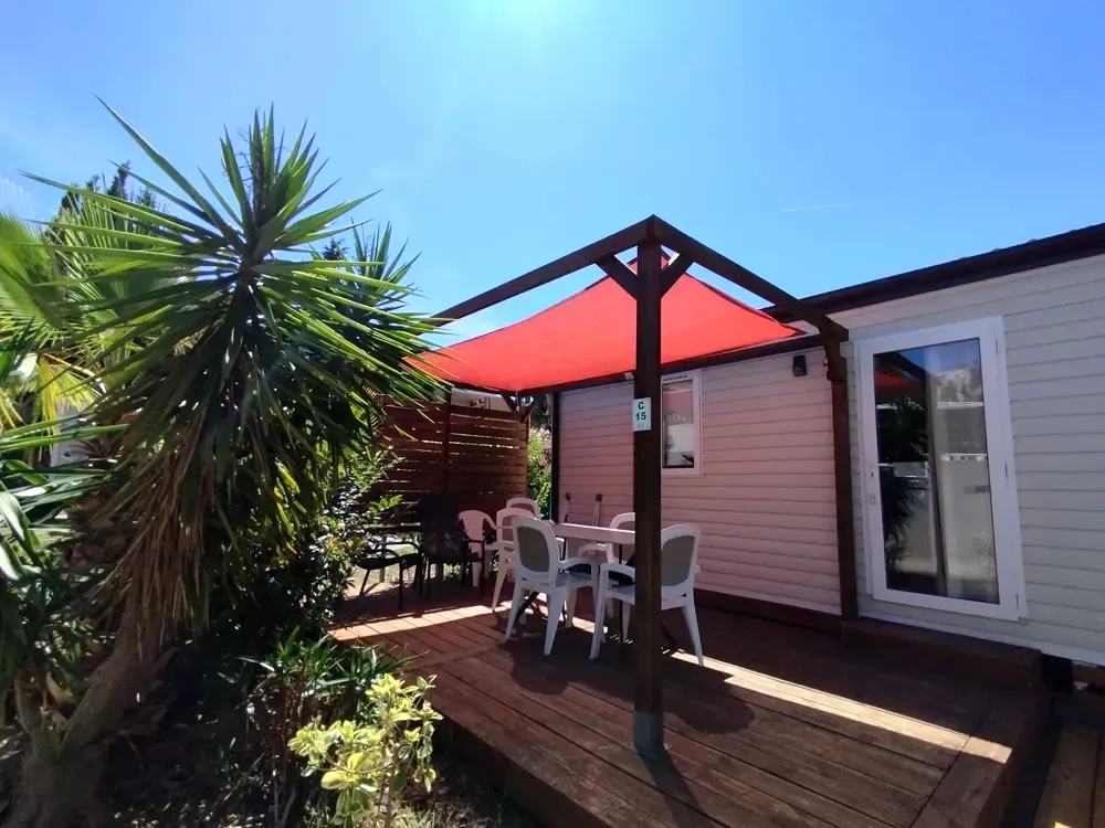 Terrasse de mobil-home ombragée par une toile rouge avec un salon de jardin blanc.