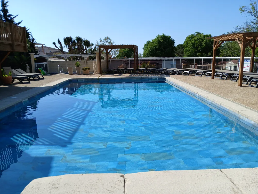Main outdoor swimming pool with aligned loungers and pergolas under a blue sky
