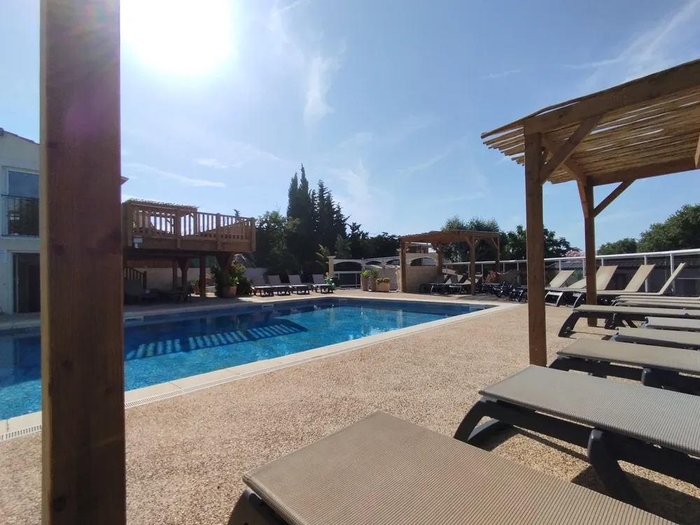 Campsite pool deck shaded by wooden pergolas with a view of the main swimming pool and sun loungers.